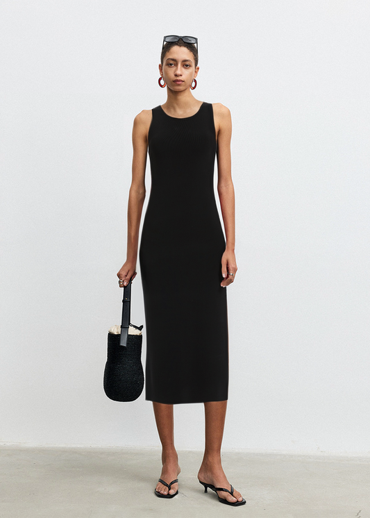 Woman wearing a black sleeveless dress holding a matching handbag against a white background